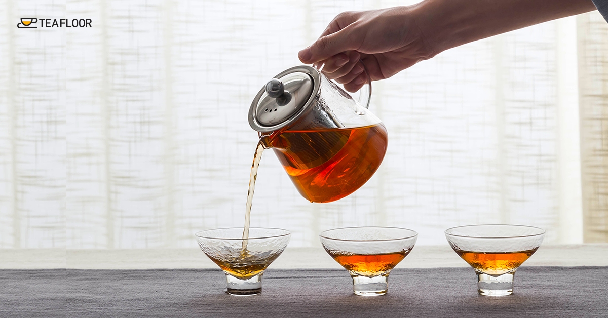 Hand pouring brewed loose leaf Darjeeling black tea into a glass cup